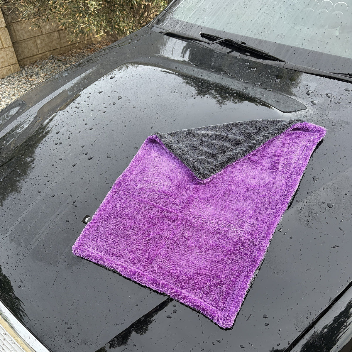 RB Innovations 1300GSM microfibre drying towel laid on a wet black bonnet, purple side up with the black corner folded back